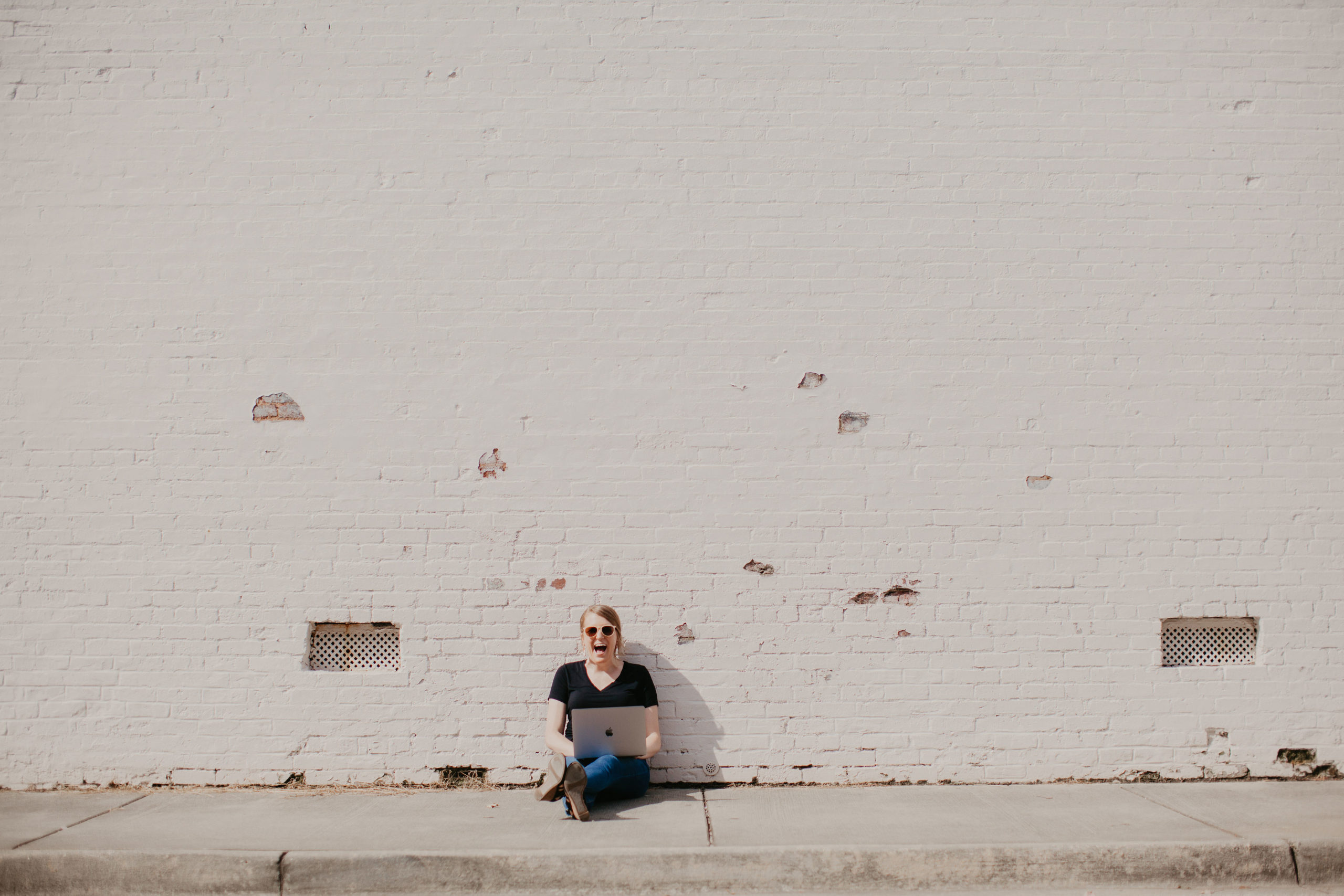 Diana P. Carter sitting against white brick wall with laptop in Charlotte, NC