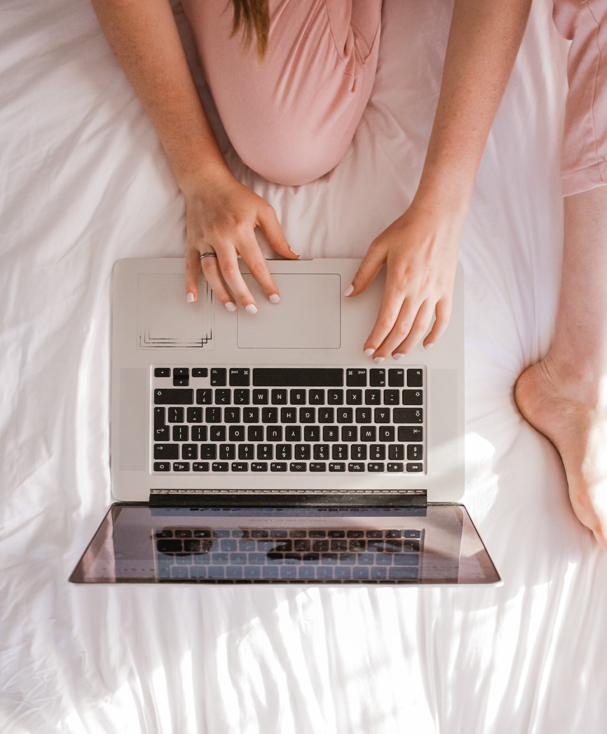 Girl in pink pants looking at laptop on white bedspread